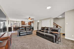 Carpeted living room featuring ceiling fan with notable chandelier