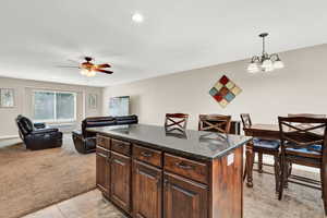 Kitchen featuring ceiling fan with notable chandelier, light carpet, dark stone counters, pendant lighting, and a kitchen island