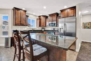 Kitchen featuring dark stone counters, sink, a center island, a breakfast bar, and appliances with stainless steel finishes