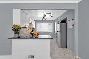 Kitchen with white cabinets, backsplash, stainless steel refrigerator, sink, and kitchen peninsula