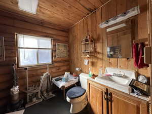 Bathroom featuring vanity, toilet, rustic walls, and wooden ceiling