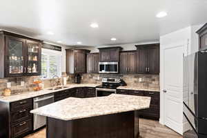 Kitchen with a kitchen island, dark brown cabinets, light hardwood / wood-style flooring, appliances with stainless steel finishes, and sink