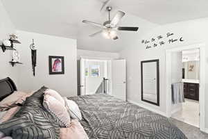 Bedroom with ensuite bath, vaulted ceiling, light carpet, and ceiling fan