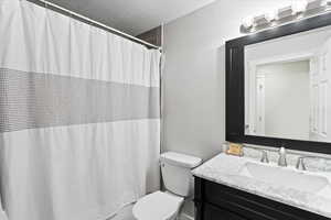 Bathroom featuring a textured ceiling, vanity, toilet, and curtained shower