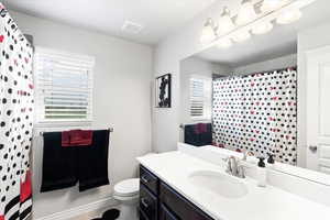 Bathroom with a shower with curtain, vanity, toilet, and plenty of natural light