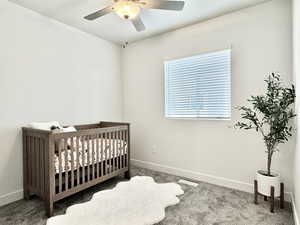 Carpeted bedroom featuring ceiling fan and a crib