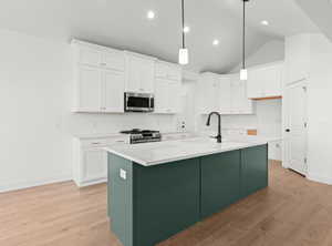 Kitchen featuring light wood-type flooring, stainless steel appliances, white cabinetry, and a center island with sink