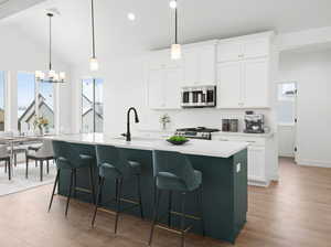 Kitchen with lofted ceiling, a center island with sink, white cabinets, light hardwood / wood-style floors, and stainless steel appliances