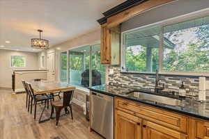 Kitchen with dark stone counters, backsplash, decorative light fixtures, dishwasher, and light hardwood / wood-style floors