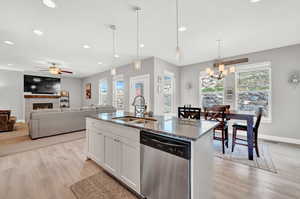 Kitchen with stone counters, ceiling fan with notable chandelier, white cabinetry, sink, and stainless steel dishwasher