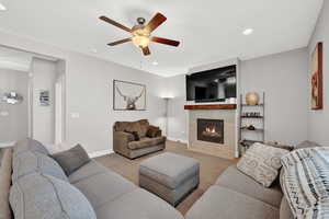 Carpeted living room with ceiling fan and a tiled fireplace