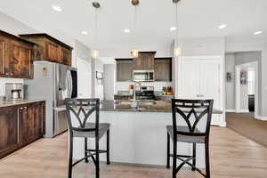 Kitchen with pendant lighting, dark stone countertops, dark brown cabinetry, and appliances with stainless steel finishes