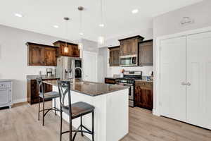 Kitchen with light wood-type flooring, decorative light fixtures, stainless steel appliances, sink, and a kitchen island with sink