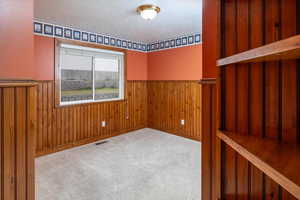 Bedroom #3 featuring light colored carpet, a textured ceiling, and wood walls