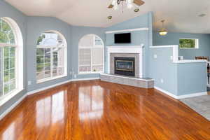 Unfurnished living room with a wealth of natural light, a tiled fireplace, ceiling fan, and hardwood / wood-style flooring