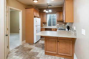 2nd Kitchen featuring white refrigerator, a notable chandelier, kitchen peninsula, hanging light fixtures, and crown molding