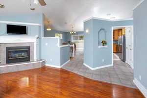 Unfurnished living room with light hardwood / wood-style floors, ceiling fan with notable chandelier, vaulted ceiling, a fireplace, and crown molding