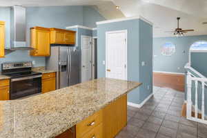 Kitchen with appliances with stainless steel finishes, light stone counters, wall chimney exhaust hood, lofted ceiling, and ceiling fan