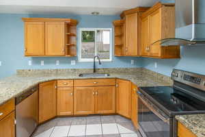 Kitchen with light tile patterned flooring, light stone counters, stainless steel appliances, sink, and wall chimney range hood