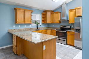 Kitchen with kitchen peninsula, sink, wall chimney range hood, appliances with stainless steel finishes, and vaulted ceiling