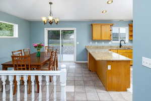 Kitchen with pendant lighting, light stone counters, a chandelier, light tile patterned flooring, and sink