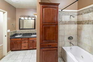 Bathroom with a textured ceiling, tiled shower / bath combo, vanity, and tile patterned floors