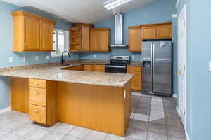 Kitchen with appliances with stainless steel finishes, wall chimney exhaust hood, vaulted ceiling, and kitchen peninsula