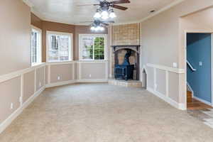 Unfurnished living room featuring a wood stove, carpet, ceiling fan, and crown molding