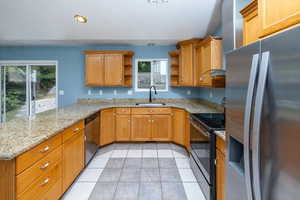 Kitchen with light stone counters, light tile patterned floors, sink, kitchen peninsula, and stainless steel appliances