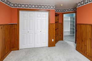 Bedroom #3 featuring a textured ceiling, wood walls, light carpet, and a closet