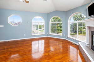 Unfurnished living room featuring a fireplace, vaulted ceiling, hardwood / wood-style floors, and plenty of natural light