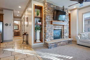 Carpeted living room with ceiling fan, a fireplace, and crown molding