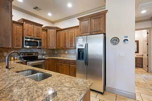 Kitchen with crown molding, appliances with stainless steel finishes, light stone counters, sink, and decorative backsplash