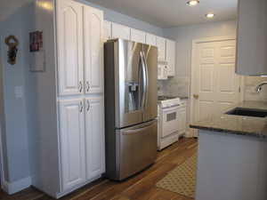 Kitchen featuring dark hardwood / wood-style floors, white appliances, sink, dark stone countertops, and white cabinets