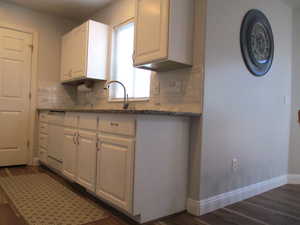 Kitchen with backsplash, stone counters, dark hardwood / wood-style flooring, white cabinetry, and sink