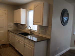 Kitchen with dark stone counters, white cabinetry, sink, and dark hardwood / wood-style floors