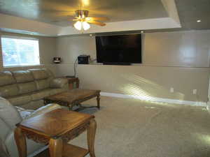 Carpeted living room with a tray ceiling and ceiling fan