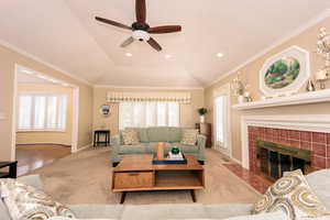 Carpeted living room featuring lofted ceiling, ceiling fan, a fireplace, and crown molding