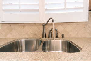 Room details featuring light stone counters, sink, and decorative backsplash