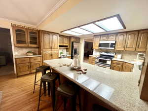 Kitchen with appliances with stainless steel finishes, light wood-type flooring, a kitchen breakfast bar, crown molding, and decorative backsplash