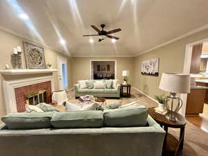 Living room with lofted ceiling, a tiled fireplace, ornamental molding, and light hardwood / wood-style floors