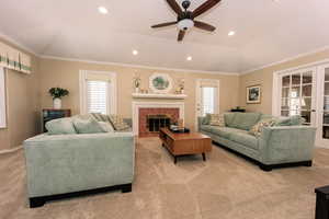 Carpeted living room featuring ceiling fan, a fireplace, and ornamental molding