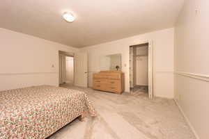 Carpeted bedroom featuring a textured ceiling, a walk in closet, and a closet