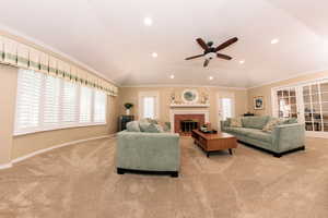 Carpeted living room with a fireplace, vaulted ceiling, crown molding, and ceiling fan