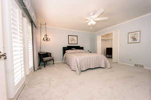 Primary bedroom with a closet, ceiling fan, light colored carpet, and ornamental molding