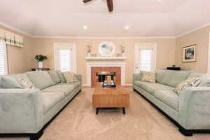 Living room featuring a fireplace, ornamental molding, ceiling fan, vaulted ceiling, and light colored carpet