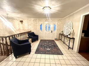 Foyer entrance with crown molding, a notable chandelier, and light tile patterned floors