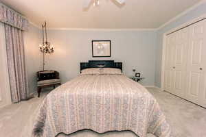 Primary carpeted bedroom with ornamental molding, ceiling fan with notable chandelier, and a closet