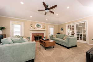 Living room with light carpet, crown molding, ceiling fan, and a tile fireplace