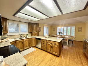 Kitchen featuring kitchen peninsula, stainless steel dishwasher, light wood-type flooring, sink, and decorative light fixtures